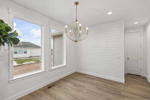 Unfurnished dining area with wood finished floors, a healthy amount of sunlight, baseboards, and a notable chandelier