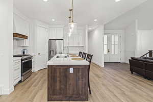 Kitchen featuring light countertops, a sink, light wood-type flooring, pendant lighting, and appliances with stainless steel finishes