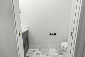 Half bath featuring baseboards, tile patterned floors, vanity, and toilet