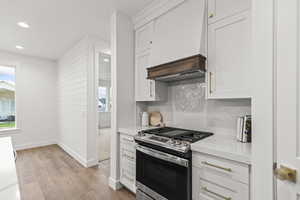Kitchen featuring decorative backsplash, light countertops, light wood-style flooring, baseboards, and stainless steel gas range oven