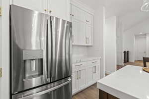 Kitchen featuring white cabinetry, light stone counters, light wood-type flooring, and stainless steel fridge