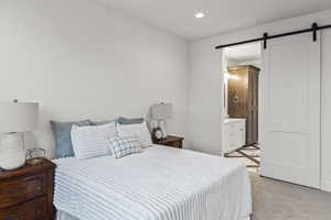 Bedroom with light carpet, a sink, a barn door, recessed lighting, and ensuite bath