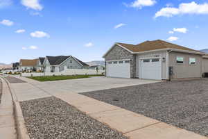 View of side of home featuring a garage, concrete driveway, a mountain view, stone siding, and a residential view