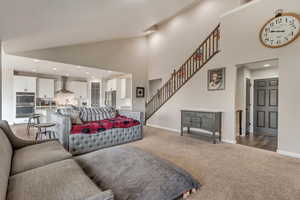 Living area with baseboards, carpet, high vaulted ceiling, and stairway