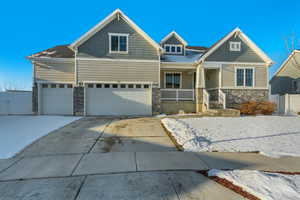 View of front of house featuring driveway, a porch, stone siding, fence, and a garage