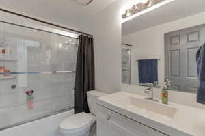Full bath with combined bath / shower with glass door, toilet, and vanity
