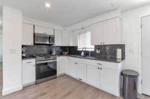 Kitchen with light wood-type flooring, white cabinets, a sink, and appliances with stainless steel finishes