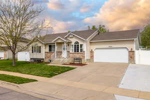 View of front facade with an attached garage, driveway, brick siding, and a front yard
