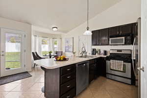 Kitchen with vaulted ceiling, a sink, light tile patterned flooring, a peninsula, and appliances with stainless steel finishes