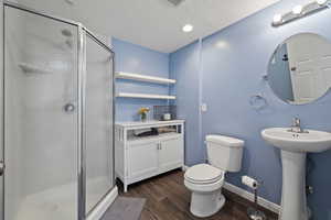 Full bath featuring toilet, a sink, wood finished floors, a stall shower, and baseboards