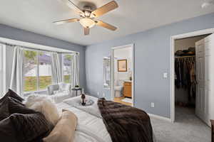 Bedroom with a closet, a spacious closet, light carpet, baseboards, and ensuite bath