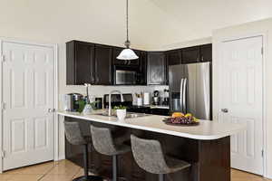 Kitchen featuring a kitchen breakfast bar, light tile patterned floors, stainless steel appliances, light countertops, and a peninsula