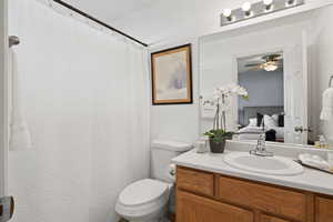 Ensuite bathroom with vanity, connected bathroom, ceiling fan, and toilet