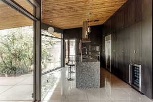 Kitchen with dark stone countertops, wine cooler, wooden ceiling, a sink, and built in appliances