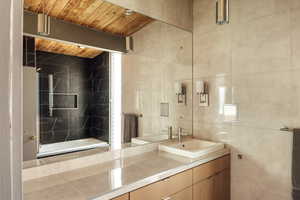 Bathroom featuring tiled shower / bath combo, tile walls, vanity, and wood ceiling