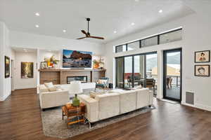 Living room featuring dark wood finished floors, a glass covered fireplace, baseboards, recessed lighting, and a ceiling fan