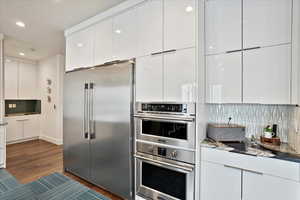 Kitchen featuring stainless steel appliances, modern cabinets, backsplash, and dark wood finished floors