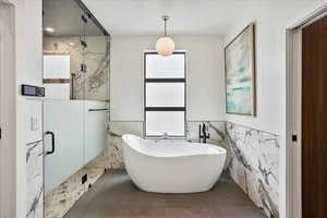 Bathroom featuring a freestanding bath, tile walls, a marble finish shower, and wainscoting