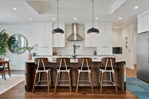 Kitchen with wall chimney exhaust hood, stainless steel built in refrigerator, baseboards, modern cabinets, and decorative backsplash