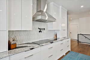 Kitchen featuring wall chimney range hood, tasteful backsplash, modern cabinets, dark wood finished floors, and white cabinetry