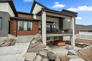 Rear view of property with fence, a hot tub, a patio area, and a balcony