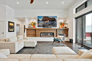 Living area with dark wood-type flooring, a glass covered fireplace, a ceiling fan, and recessed lighting
