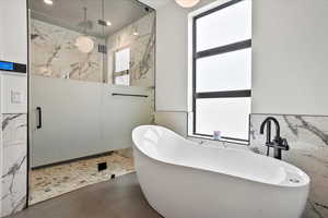 Bathroom with a freestanding bath, a healthy amount of sunlight, a marble finish shower, and tile walls