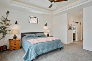 Carpeted bedroom featuring a barn door, baseboards, crown molding, and a raised ceiling