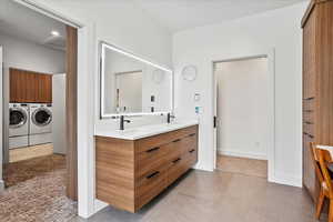 Bathroom with double vanity, tile patterned floors, washer and dryer, and a sink