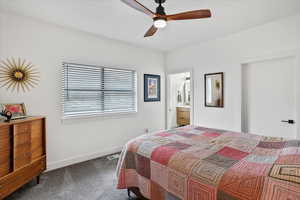 Carpeted bedroom with visible vents, ensuite bathroom, baseboards, and ceiling fan