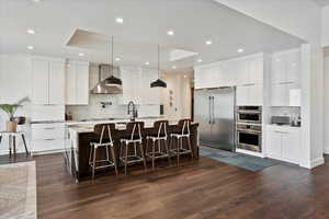 Kitchen with modern cabinets, wall chimney range hood, backsplash, and appliances with stainless steel finishes