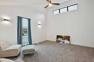 Carpeted living area featuring ceiling fan and baseboards