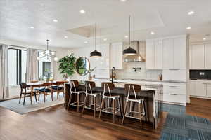 Kitchen featuring wall chimney range hood, decorative backsplash, and modern cabinets