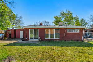 Back of house with fence, a chimney, brick siding, and a yard