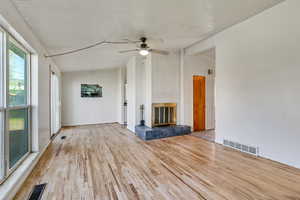 Unfurnished living room featuring wood finished floors, visible vents, a fireplace, and ceiling fan