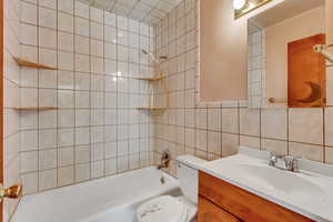 Bathroom with tasteful backsplash, shower / bathing tub combination, vanity, tile walls, and toilet