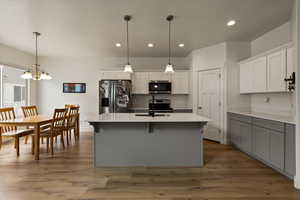 Kitchen featuring a sink, an island with sink, a chandelier, light countertops, and appliances with stainless steel finishes
