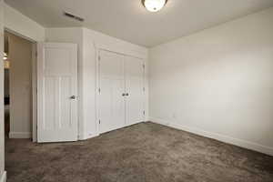 Unfurnished bedroom featuring a closet, dark carpet, visible vents, and baseboards