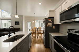 Kitchen with a sink, pendant lighting, stainless steel appliances, light countertops, and a notable chandelier