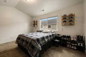 Carpeted bedroom featuring vaulted ceiling, visible vents, and baseboards