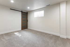 Basement featuring baseboards, visible vents, carpet flooring, and a barn door
