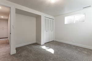 Unfurnished bedroom with carpet floors, a textured ceiling, visible vents, and baseboards