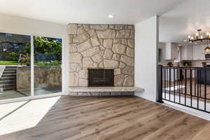 Unfurnished living room featuring wood finished floors, a textured ceiling, a fireplace, baseboards, and a notable chandelier