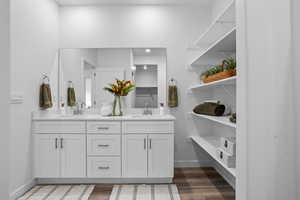 Bathroom featuring double vanity, baseboards, wood finished floors, and a sink