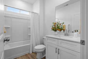 Full bathroom with wood finished floors, vanity, shower / bath combination with curtain, toilet, and visible vents