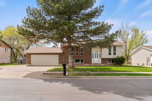 Raised ranch with brick siding, a front lawn, driveway, and a garage