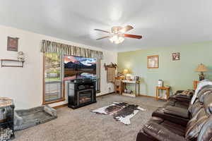 Carpeted living area featuring a glass covered fireplace, a ceiling fan, and baseboards