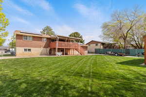 Back of property featuring fence, a wooden deck, a patio area, stairway, and roof mounted solar panels