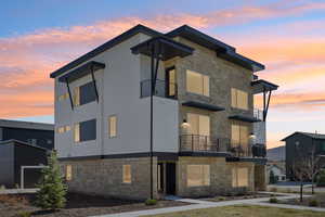Property exterior at dusk featuring stone siding and a balcony