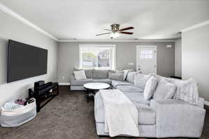 Living room featuring dark colored carpet, baseboards, ornamental molding, and a ceiling fan